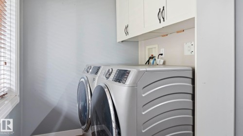 Dedicated laundry area featuring overhead cabinetry, a window with horizontal blinds, and light-toned walls - 10115 104 Street, Westlock, AB 