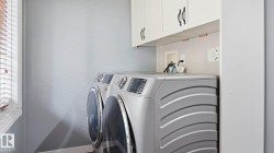 Dedicated laundry area featuring overhead cabinetry, a window with horizontal blinds, and light-toned walls - 
