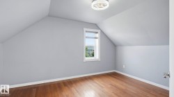 Room featuring wood-finish flooring, a contemporary ceiling light fixture, and a window with a roller shade - 