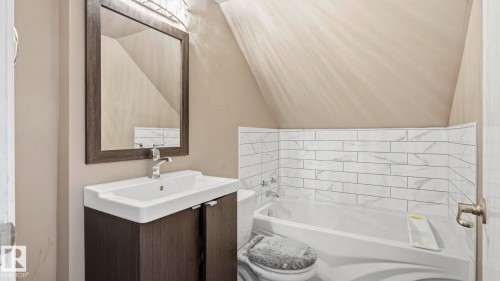 Bathroom featuring a modern vanity with integrated sink, framed mirror, and a built-in bathtub with subway tile surround - 10115 104 Street, Westlock, AB 