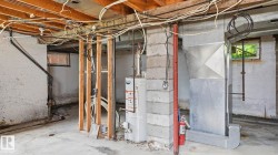 Unfinished basement featuring exposed wood joists, concrete block walls, a water heater, and visible ductwork - 