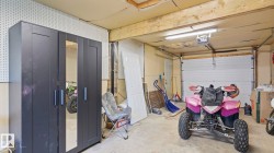 Garage space with overhead lighting, a white sectional garage door, exposed ceiling joists, and a side access door - 