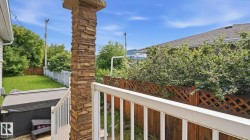 Stacked stone pillar and white railing leading to an outdoor space featuring a covered hot tub, green lawn, and white picket fencing - 