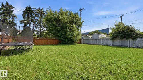 Expansive green space featuring a wooden fence, mature trees, and a clear blue sky - 10115 104 Street, Westlock, AB 