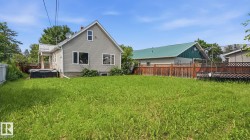 Expansive rear yard featuring green space, a grey-sided residence with white trim, and a partially covered back porch - 