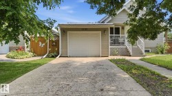 Attached garage with overhead door, concrete driveway, front porch with white railing, light-colored siding, and a gabled roofline - 