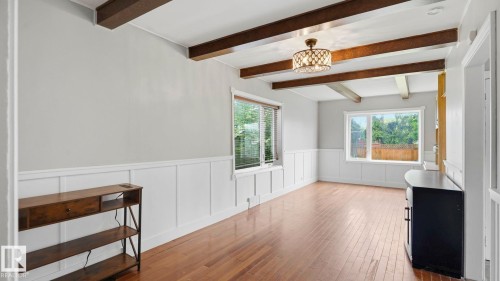 Spacious room featuring wood-finish flooring, white wainscoting, exposed ceiling beams, and multiple windows providing natural illumination - 10115 104 Street, Westlock, AB 