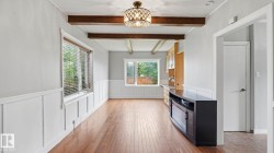 Open concept room featuring wood-finish flooring, white wainscoting, exposed ceiling beams, and a decorative semi-flush mount light fixture - 