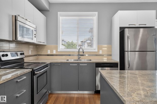 Modern kitchen featuring stainless steel appliances, wood-finish flooring, light grey and white cabinetry, stone countertops, and a subway tile backsplash - 24 655 Watt Boulevard, Edmonton, AB 