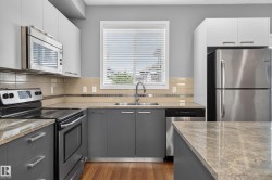 Modern kitchen featuring stainless steel appliances, wood-finish flooring, light grey and white cabinetry, stone countertops, and a subway tile backsplash - 