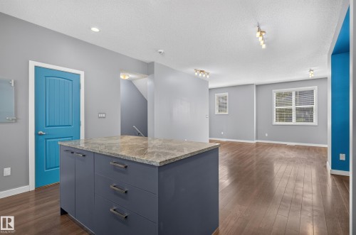 Kitchen island with a light-colored countertop and dark-toned cabinetry, set within an open-concept space featuring wood-finish flooring, recessed lighting, and track lighting fixtures - 24 655 Watt Boulevard, Edmonton, AB 