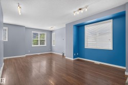 Spacious room featuring wood-finish flooring, track lighting, multiple windows with blinds, and contrasting accent walls - 