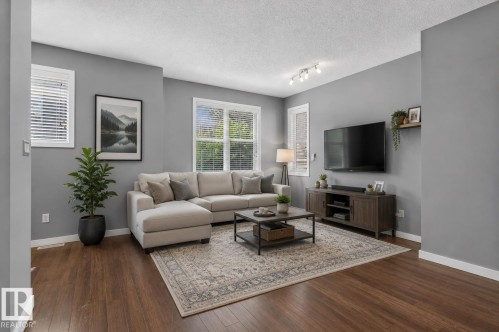 Spacious living area featuring wood-finish flooring, multiple windows with blinds, track lighting, and a neutral color palette - 24 655 Watt Boulevard, Edmonton, AB 