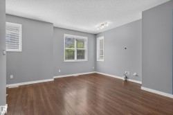 Spacious room featuring wood-finish flooring, light grey walls, white baseboards, and multiple windows with blinds - 