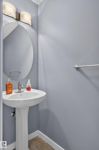 Pedestal sink with chrome faucet, oval mirror, and wall-mounted light fixture - 24 655 Watt Boulevard, Edmonton, AB 