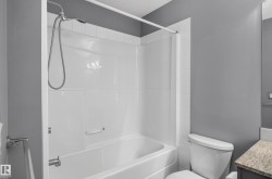 White bath and shower combination with a curved shower curtain rod, chrome fixtures, and a white toilet - 