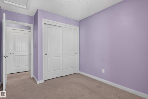 Carpeted room with lavender walls featuring white trim, a double sliding closet door, and a white interior door with a rounded top panel - 24 655 Watt Boulevard, Edmonton, AB 