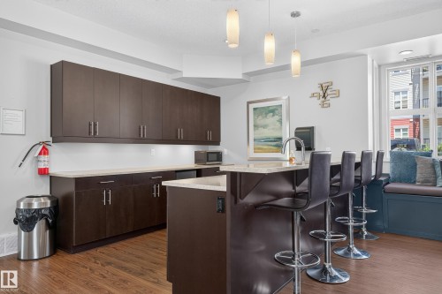 Kitchenette with extensive dark wood-finish cabinetry, light-toned countertops, and wood-finish flooring - 24 655 Watt Boulevard, Edmonton, AB 