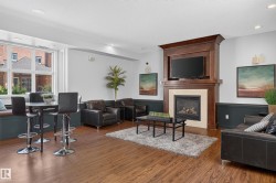 Living area featuring a rich wood-finish floor, a built-in fireplace with a light-toned surround, a prominent dark wood mantelpiece, recessed ceiling lighting, and a large multi-pane window - 