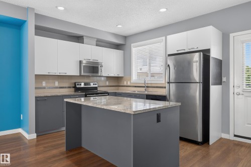 Kitchen featuring a central island with a light-toned countertop, two-tone cabinetry, stainless steel appliances, wood-finish flooring, and recessed lighting - 24 655 Watt Boulevard, Edmonton, AB 