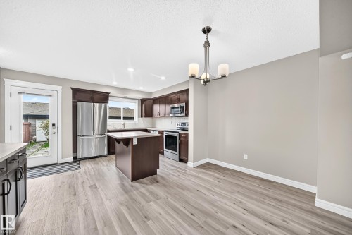 Kitchen and dining area featuring wood-finish flooring, dark wood cabinetry, stainless steel appliances, a center island, and a contemporary chandelier - 69 Tonewood Boulevard, Spruce Grove, AB - Indoor Photo Showing Kitchen With Upgraded Kitchen