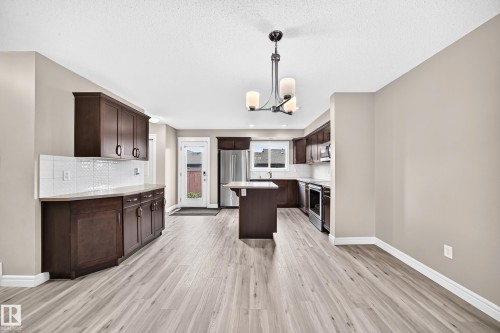 Open-concept kitchen featuring dark wood cabinetry, stainless steel appliances, a central island, and wood-finish flooring - 69 Tonewood Boulevard, Spruce Grove, AB - Indoor