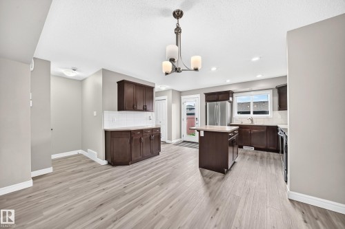 Spacious kitchen featuring wood-finish flooring, dark wood cabinetry, a central island, stainless steel refrigerator, and white subway tile backsplash - 69 Tonewood Boulevard, Spruce Grove, AB - Indoor Photo Showing Kitchen