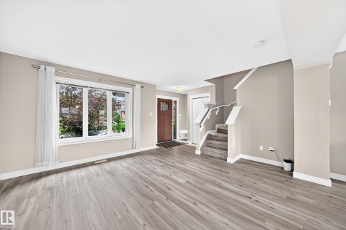Spacious living area featuring light wood-finish flooring, a large window with white trim, and neutral wall tones - 69 Tonewood Boulevard, Spruce Grove, AB - Indoor