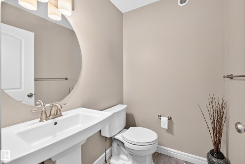 Pedestal sink with brushed nickel faucet, large circular mirror, and neutral wall tones - 69 Tonewood Boulevard, Spruce Grove, AB - Indoor Photo Showing Bathroom