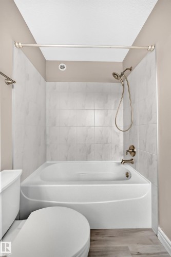 Bathroom featuring a white bathtub with a tiled surround, bronze shower fixtures, and wood-finish flooring - 69 Tonewood Boulevard, Spruce Grove, AB - Indoor Photo Showing Bathroom