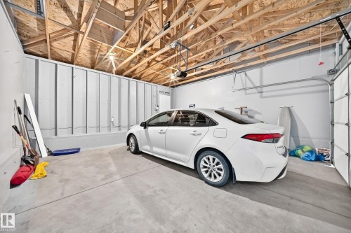 Spacious garage featuring a concrete floor, exposed wood ceiling trusses, and an automatic garage door opener - 69 Tonewood Boulevard, Spruce Grove, AB - Indoor Photo Showing Garage