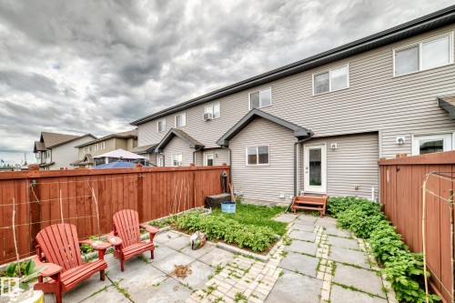 Rear exterior featuring light grey siding and multiple windows, a ground-level patio door with wood steps, a private wood fence, and a stone paver patio area - 69 Tonewood Boulevard, Spruce Grove, AB - Outdoor