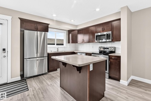 Modern kitchen featuring wood-finish flooring, dark wood cabinetry, white subway tile backsplash, and stainless steel appliances - 69 Tonewood Boulevard, Spruce Grove, AB - Indoor Photo Showing Kitchen