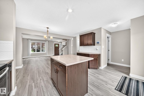 Kitchen island with light-toned countertop, dark wood-finish cabinetry, and wood-finish flooring - 69 Tonewood Boulevard, Spruce Grove, AB - Indoor Photo Showing Kitchen