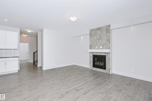 Spacious living area featuring light wood-finish flooring and a tiled fireplace with a white mantel - 1235 164 Street, Edmonton, AB 