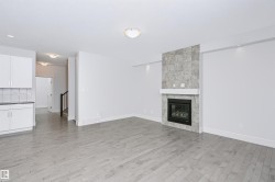 Spacious living area featuring light wood-finish flooring and a tiled fireplace with a white mantel - 
