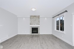 Living area featuring a floor-to-ceiling tiled fireplace with a white mantel, wood-finish flooring, and a large window with black hardware - 