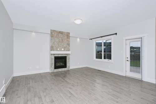 Spacious room featuring wood-finish flooring, a contemporary fireplace with a stone-tile surround, and a white mantel - 1235 164 Street, Edmonton, AB 