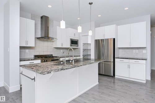 Kitchen featuring a large island with a stone-finish countertop, stainless steel appliances, white cabinetry, and wood-finish flooring - 1235 164 Street, Edmonton, AB 