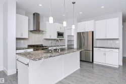 Kitchen featuring a large island with a stone-finish countertop, stainless steel appliances, white cabinetry, and wood-finish flooring - 