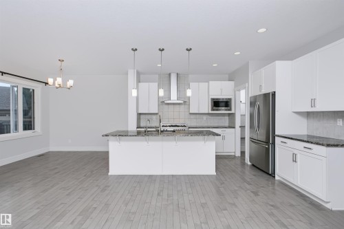 Open-concept kitchen and living area featuring light wood-finish flooring, white cabinetry, granite countertops, and stainless steel appliances - 1235 164 Street, Edmonton, AB 