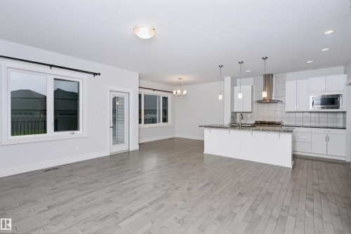 Open-concept living area featuring light wood-finish flooring, white walls, and a modern kitchen - 1235 164 Street, Edmonton, AB 
