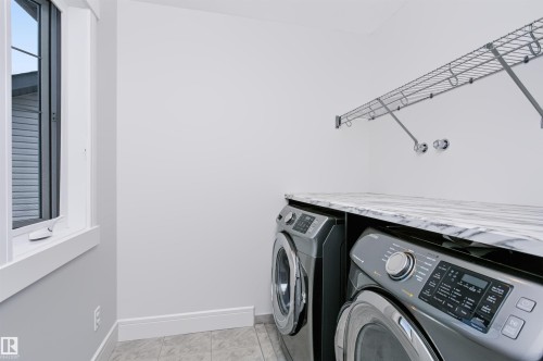 Dedicated laundry area featuring a window, built-in wire shelving, a stone-finish countertop, and tile flooring - 1235 164 Street, Edmonton, AB 