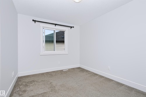 Bright room featuring neutral-toned carpet, a window with white trim, and a black curtain rod - 1235 164 Street, Edmonton, AB 