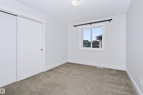 Neutral-toned bedroom featuring plush carpet flooring, white trim, and a window with a black curtain rod - 1235 164 Street, Edmonton, AB 