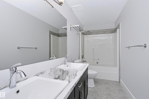 Bathroom featuring a dual vanity with undermount sinks and a marble-patterned countertop, a full-width mirror, a tub/shower combination with tile surround, and tile flooring - 1235 164 Street, Edmonton, AB 