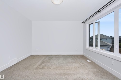Spacious room featuring neutral carpeting, white walls, and a large multi-pane window with black curtain rods - 1235 164 Street, Edmonton, AB 