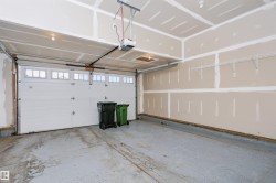 Garage space featuring a paneled overhead door with transom windows, exposed drywall, concrete flooring, overhead lighting, and an automatic door opener - 