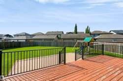 Expansive backyard featuring a wood deck with black metal railing, green lawn, and a paved walkway - 