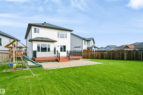 Spacious rear yard featuring a wooden privacy fence, a large deck with black railings, a paved patio area, and a bright green lawn - 1235 164 Street, Edmonton, AB 